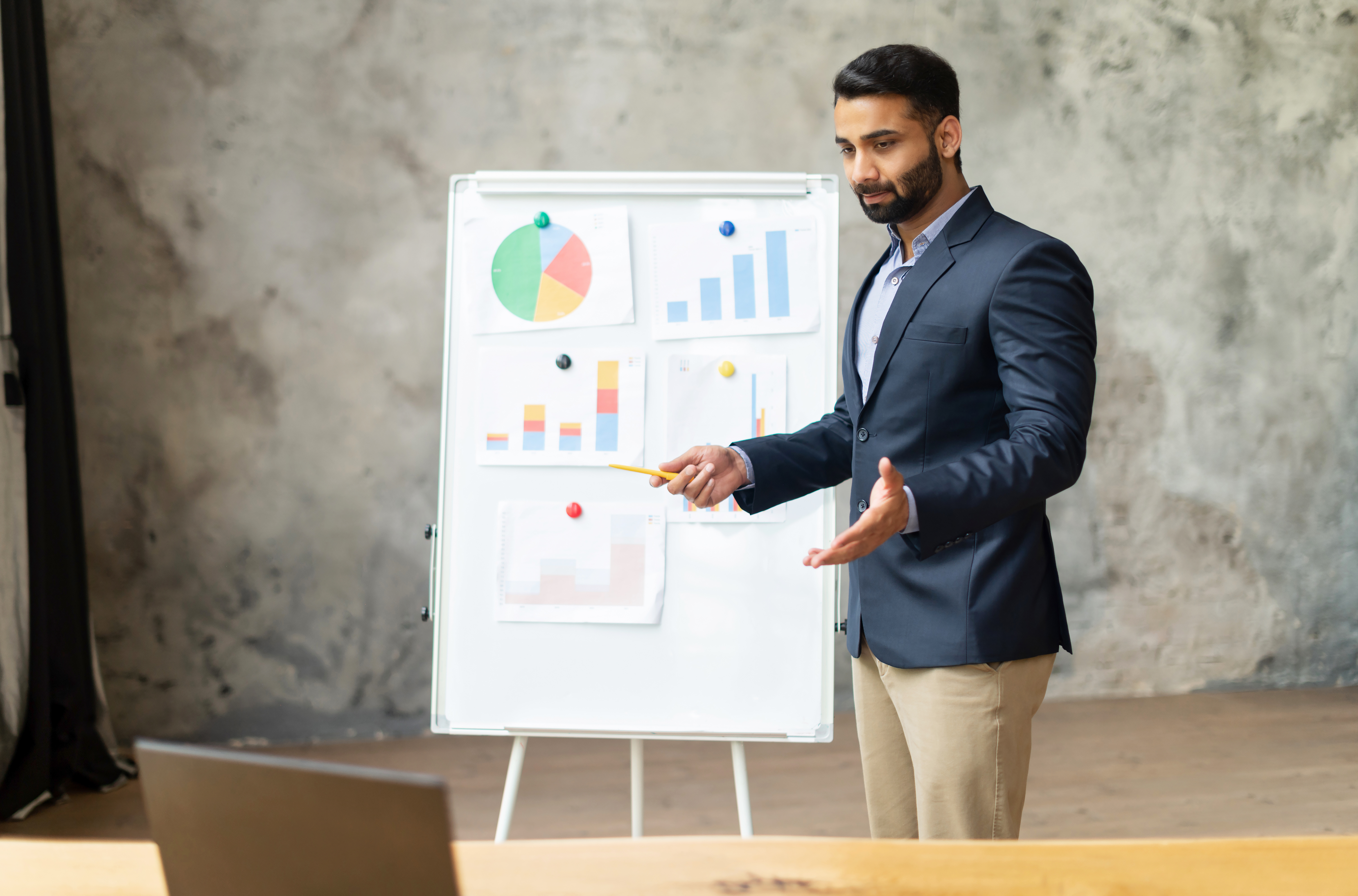 confident-indian-male-colleague-stands-near-whiteboard-front-laptop